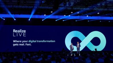 Two speakers stand on the main stage at Realize LIVE.